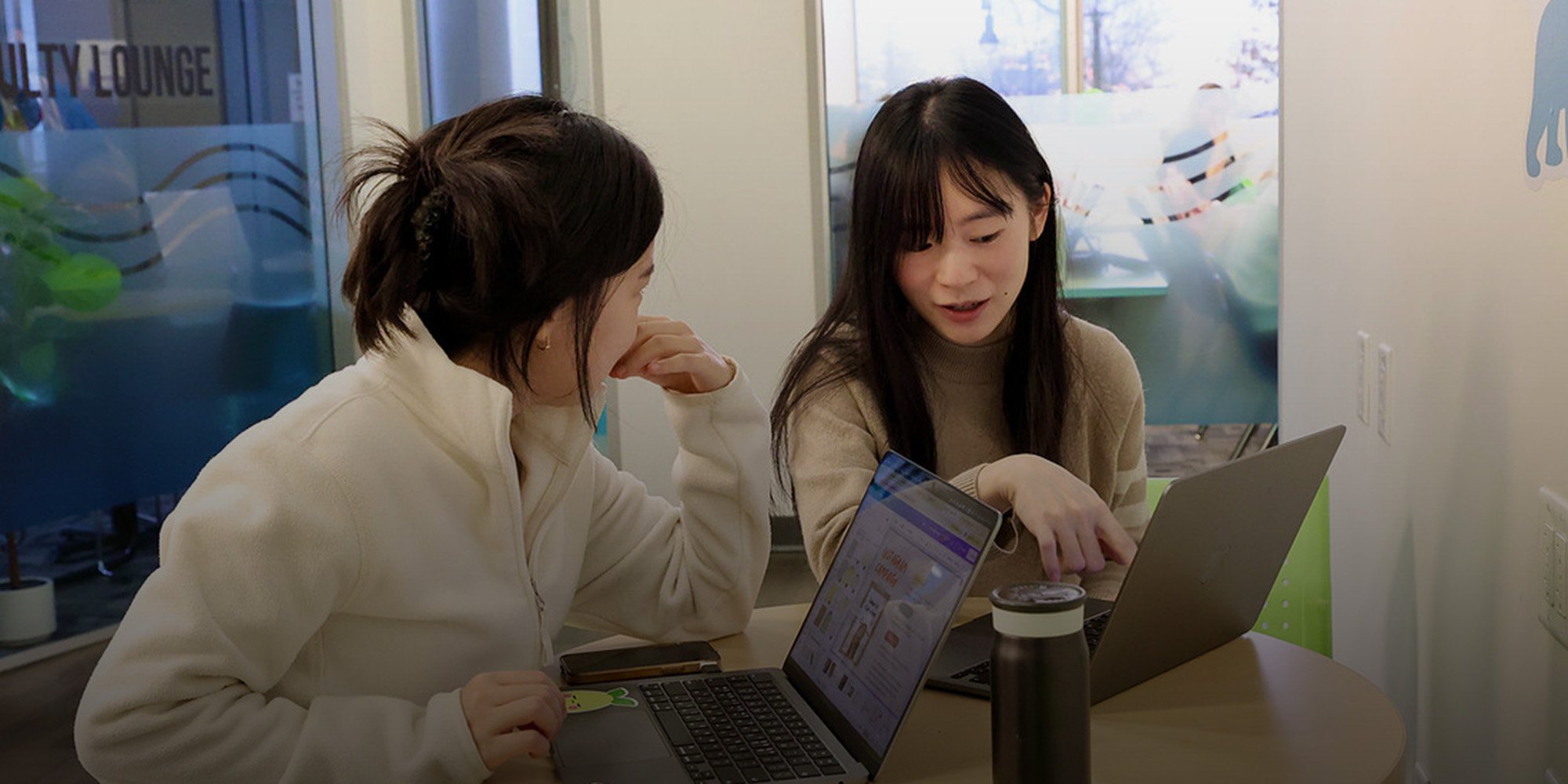 Two international students look at their laptops and talk at the ILSC Language Schools Vancouver campus
